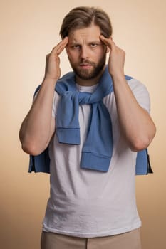 Sick ill caucasian bearded young man rubbing temples to cure headache problem, suffering from tension, migaine, stress, grimacing in pain, high blood pressure isolated alone on beige wall background