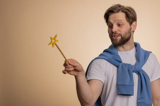 Man magician wizard gesturing with magic wand fairy stick, making wish come true, casting magician spell, advertising holidays sale discount. Young bearded guy isolated on beige studio background