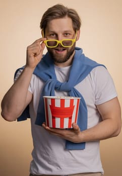 Excited caucasian man eating popcorn, watching interesting tv serial, sport game, film, online social media movie content. Young guy enjoying domestic entertainment isolated on beige studio background