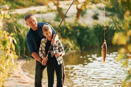 Holding the catch. Father and son on fishing together outdoors at summertime.