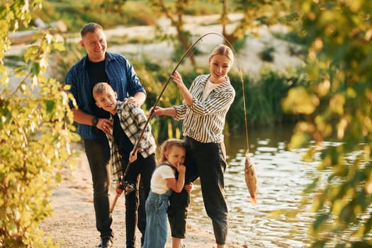 Father and mother with son and daughter on fishing together outdoors at summertime.