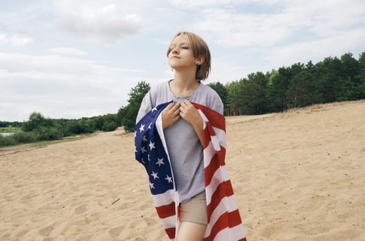 A cheerful beautiful girl is walking under the US flag, which is fluttering in the wind.