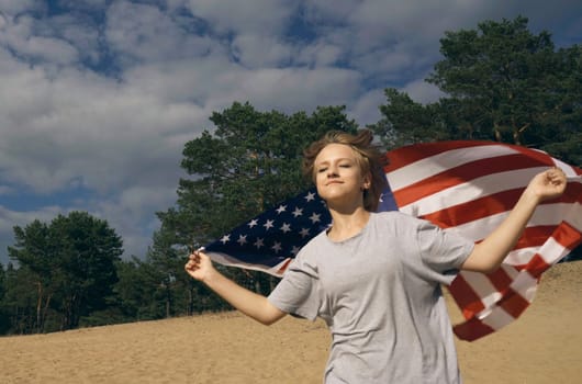 Cheerful beautiful girl runs on the sand with the USA flag.