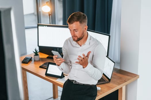 Busy day. Young businessman in formal clothes is in office with multiple screens.