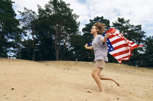 Cheerful beautiful girl runs on the sand with the USA flag. The image is blurry in motion.