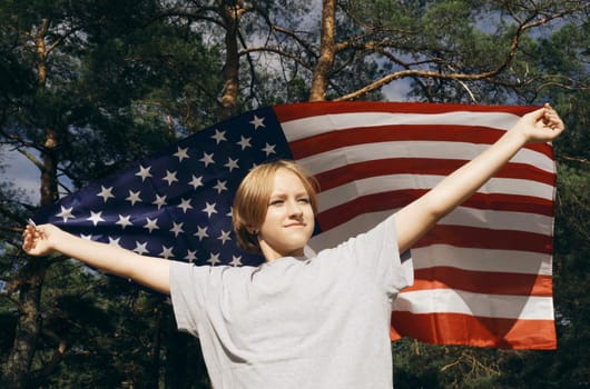 Cheerful beautiful girl stands with the flag of the USA, which flutters in the wind.