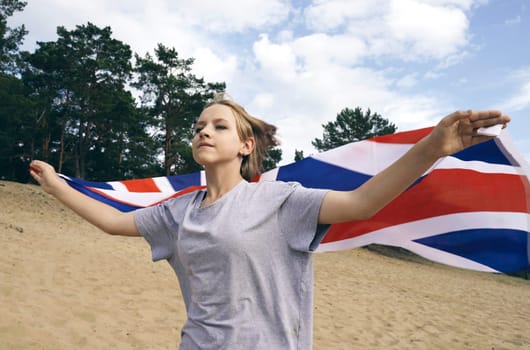 Cheerful beautiful young girl runs with the UK flag on the sand.