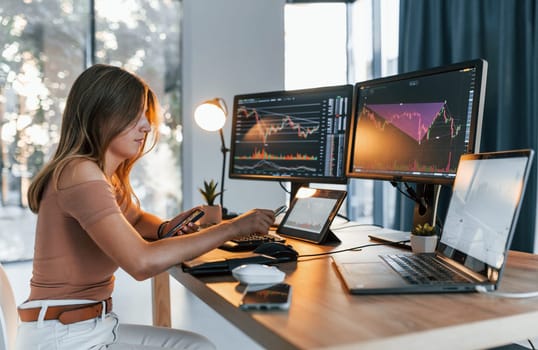 Young woman in casual clothes is in office with multiple screens.