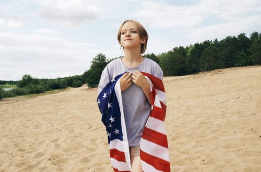 A cheerful beautiful girl is walking under the US flag, which is fluttering in the wind.