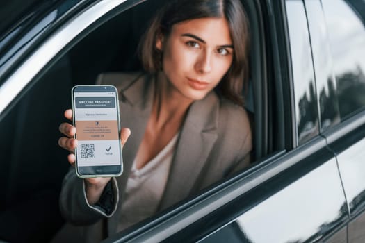 Holding vaccine passport. Woman testing new car. Sitting indoors in modern automobile.