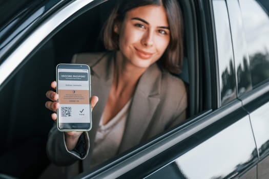 Holding vaccine passport. Woman testing new car. Sitting indoors in modern automobile.
