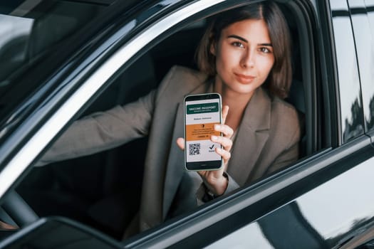 Holding vaccine passport. Woman testing new car. Sitting indoors in modern automobile.