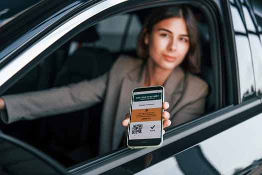 Holding vaccine passport. Woman testing new car. Sitting indoors in modern automobile.