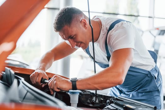 Man in uniform is repairing broken automobile indoors.