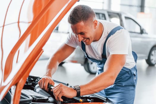 Man in uniform is repairing broken automobile indoors.