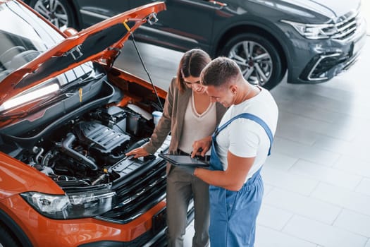 Showing results of work. Man repairing woman's automobile indoors. Professional service.