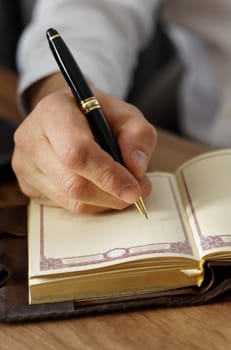 A businessman sits at a table and makes notes in a notebook. Vertical frame. Close-up.