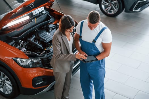 Showing results of work. Man repairing woman's automobile indoors. Professional service.