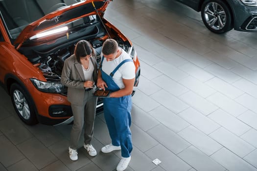 Showing results of work. Man repairing woman's automobile indoors. Professional service.