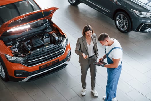 Two people. Man repairing woman's automobile indoors. Professional service.