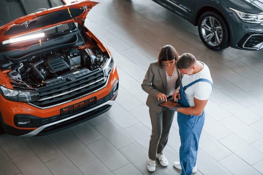 Two people. Man repairing woman's automobile indoors. Professional service.