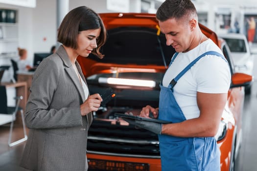 Two people. Man repairing woman's automobile indoors. Professional service.