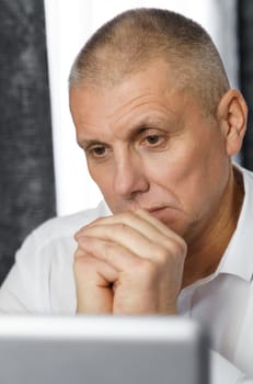 Pensive businessman, manager creates new business ideas while sitting at a table with a laptop. Vertical frame. Close-up.