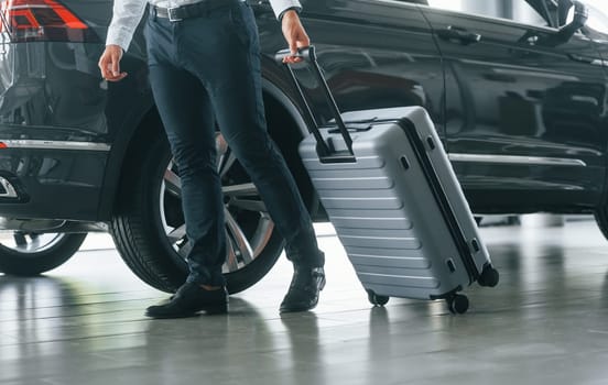 Partical view. Man in formal clothes is with luggage indoors near the car.