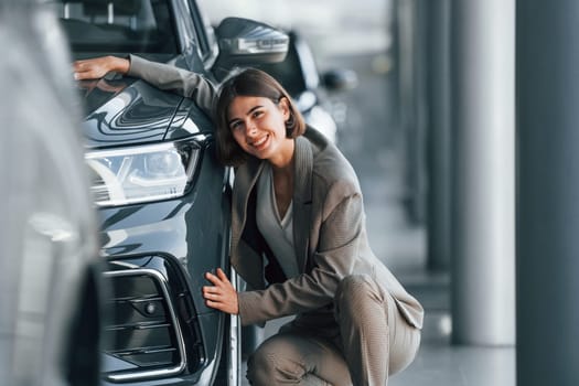 Embracing the car. Woman is indoors near brand new automobile indoors.