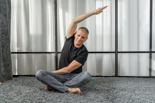 A man sits on a mat and does yoga, does exercises. Healthy lifestyle.