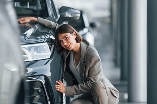 Embracing the car. Woman is indoors near brand new automobile indoors.