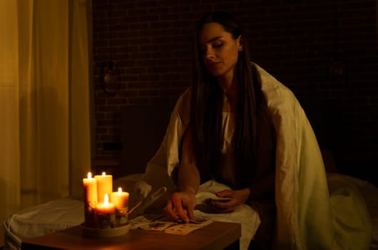 A woman fortune-telling with cards in a dark room by the light of burning candles. Image of candles in sharpness, playing cards and a woman out of focus.