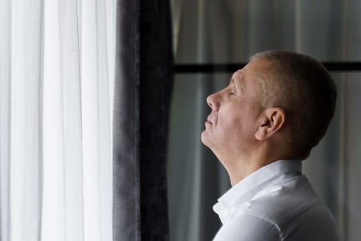 Portrait of a male businessman who stands near the window raised his head up, closed his eyes - relaxes.