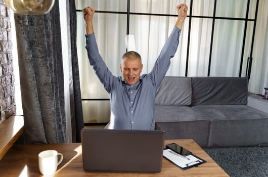 A businessman working at a computer rejoices in a perfect successful transaction, raising his hands up. The concept of success.
