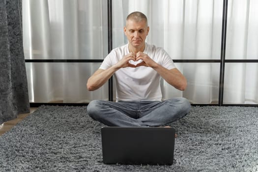Man talking on video link making heart symbol with hands in bedroom.