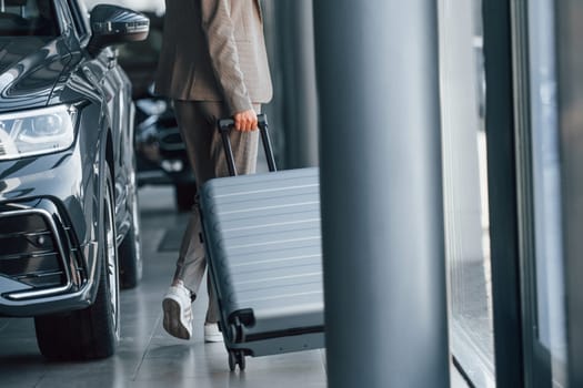 Holding luggage. Woman is indoors near brand new automobile indoors.