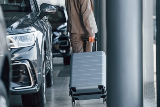 Holding luggage. Woman is indoors near brand new automobile indoors.