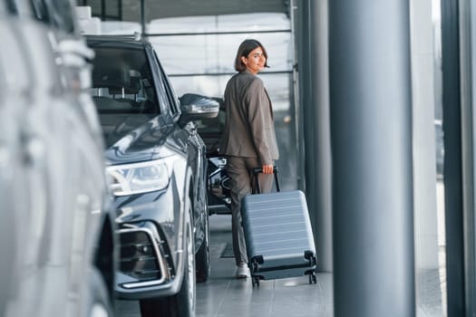 Holding luggage. Woman is indoors near brand new automobile indoors.