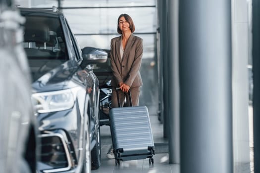 Holding luggage. Woman is indoors near brand new automobile indoors.