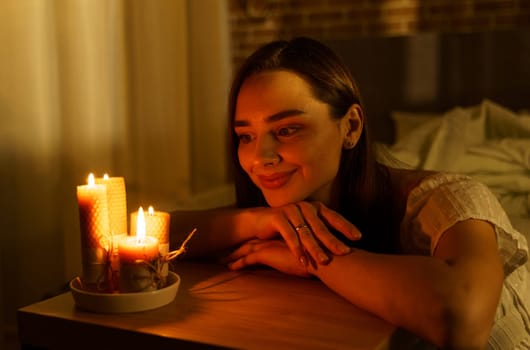 A woman holds a burning candle in her palms on a dark black background.