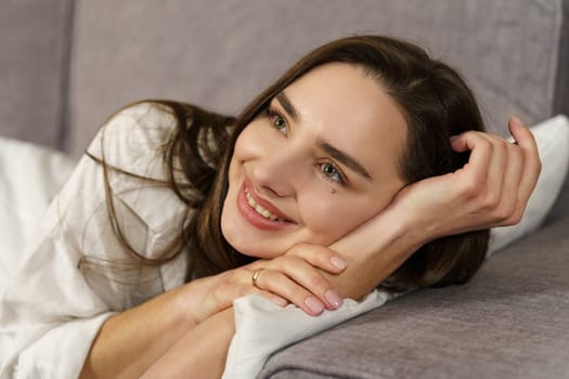 Young beautiful woman lies on the sofa watching TV, smiling.