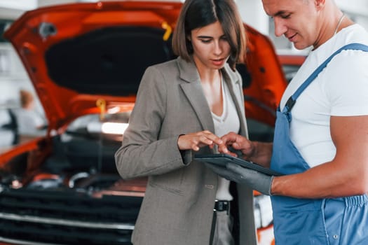 Paying for service. Man repairing woman's automobile indoors.