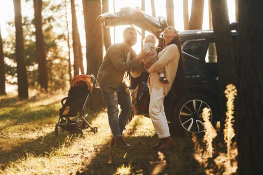 Sunlight at background. Happy family of father, mother and little daughter is in the forest.