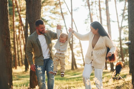 Having a walk. Happy family of father, mother and little daughter is in the forest.