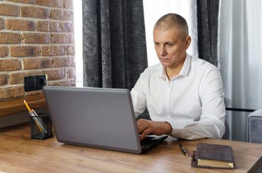 Business man, middle age, working at home with a laptop. Looking at the laptop monitor, typing. Remote business concept.