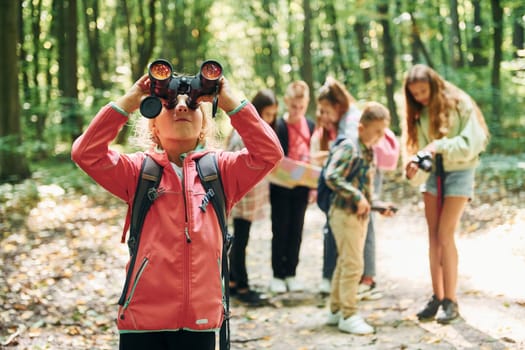 Girl looking into binoculars. Kids in green forest at summer daytime together.