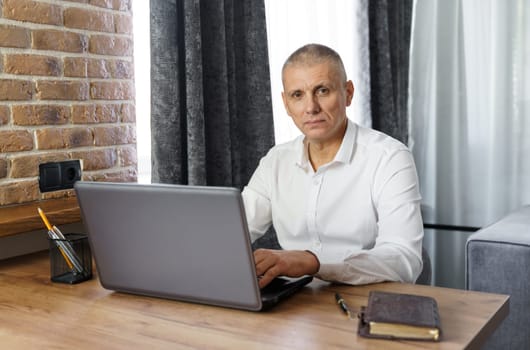 Portrait of middle aged business man working at home with laptop. Remote business concept.