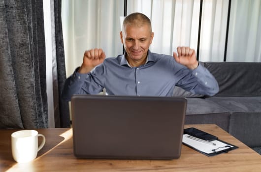 A businessman working at a computer rejoices in a perfect successful transaction, raising his hands up. The concept of success.