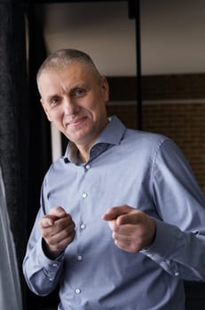 Confident smiling businessman in a blue shirt pointing with index fingers at the camera. Vertical frame. The concept of people and gestures.