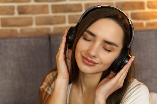 Portrait of a beautiful young woman sitting on the bed at home with headphones and listening to music. The concept of rest and relaxation.